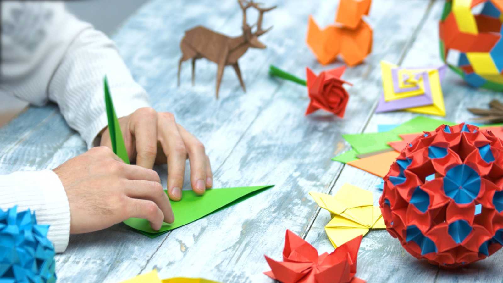 Man at origami folding lesson. Collection of beautiful origami figurines on wooden table. Traditional origami paper folding.
